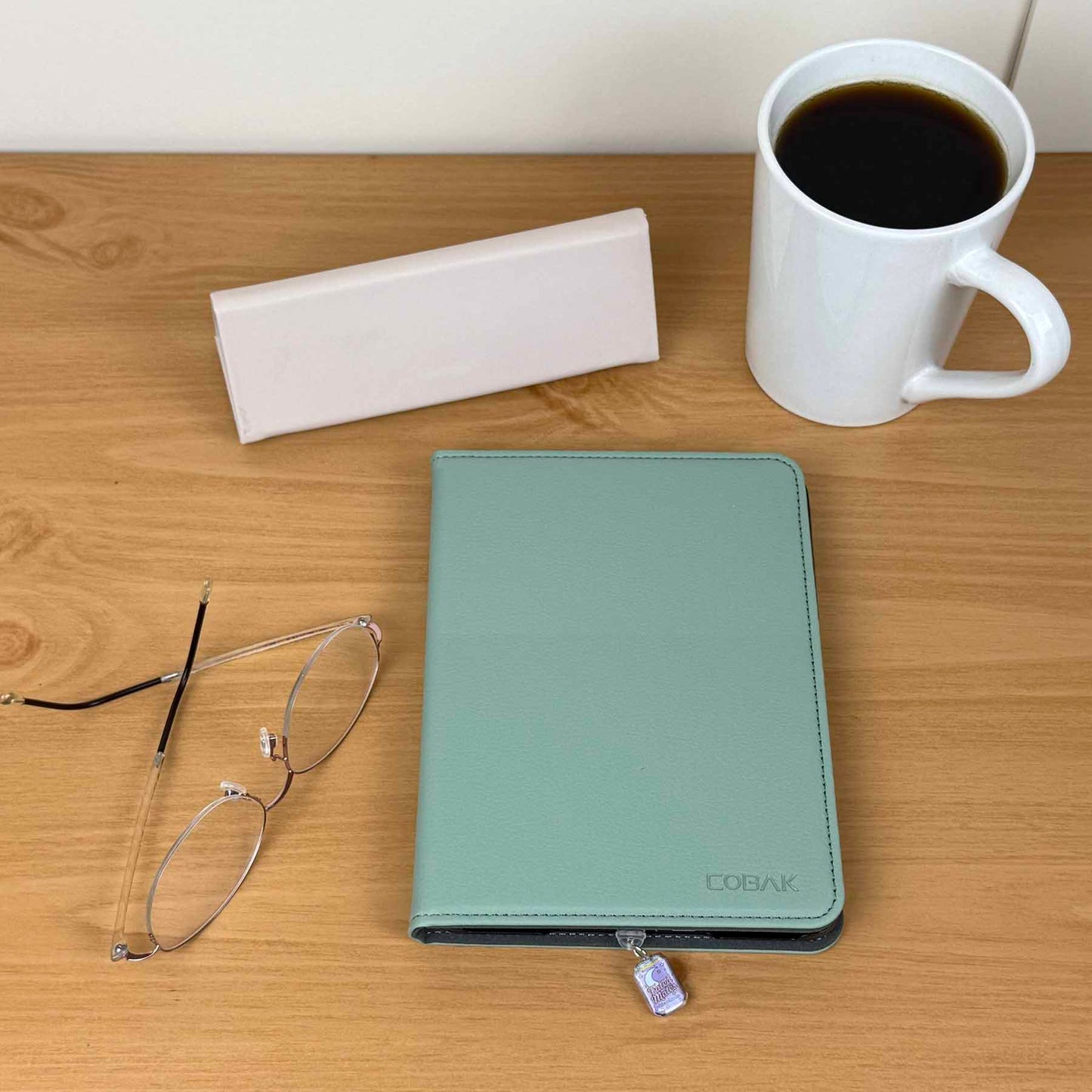 Fated Mate Soda Can Kindle Charm attached to a light blue Kindle cover, next to reading glasses and a coffee mug.