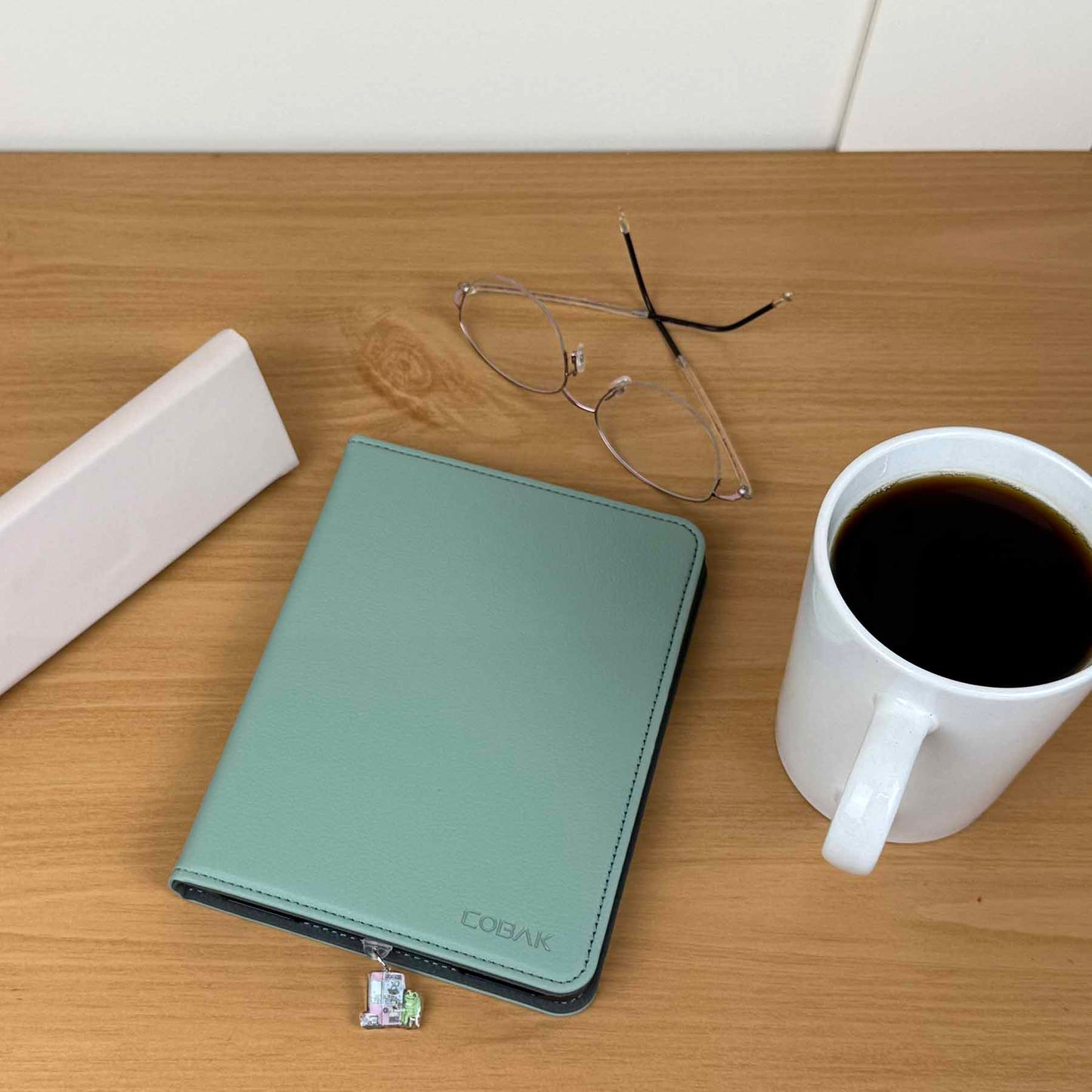 Frog & Claw Machine Kindle charm dust plug on a green Kindle cover next to glasses and a coffee mug.