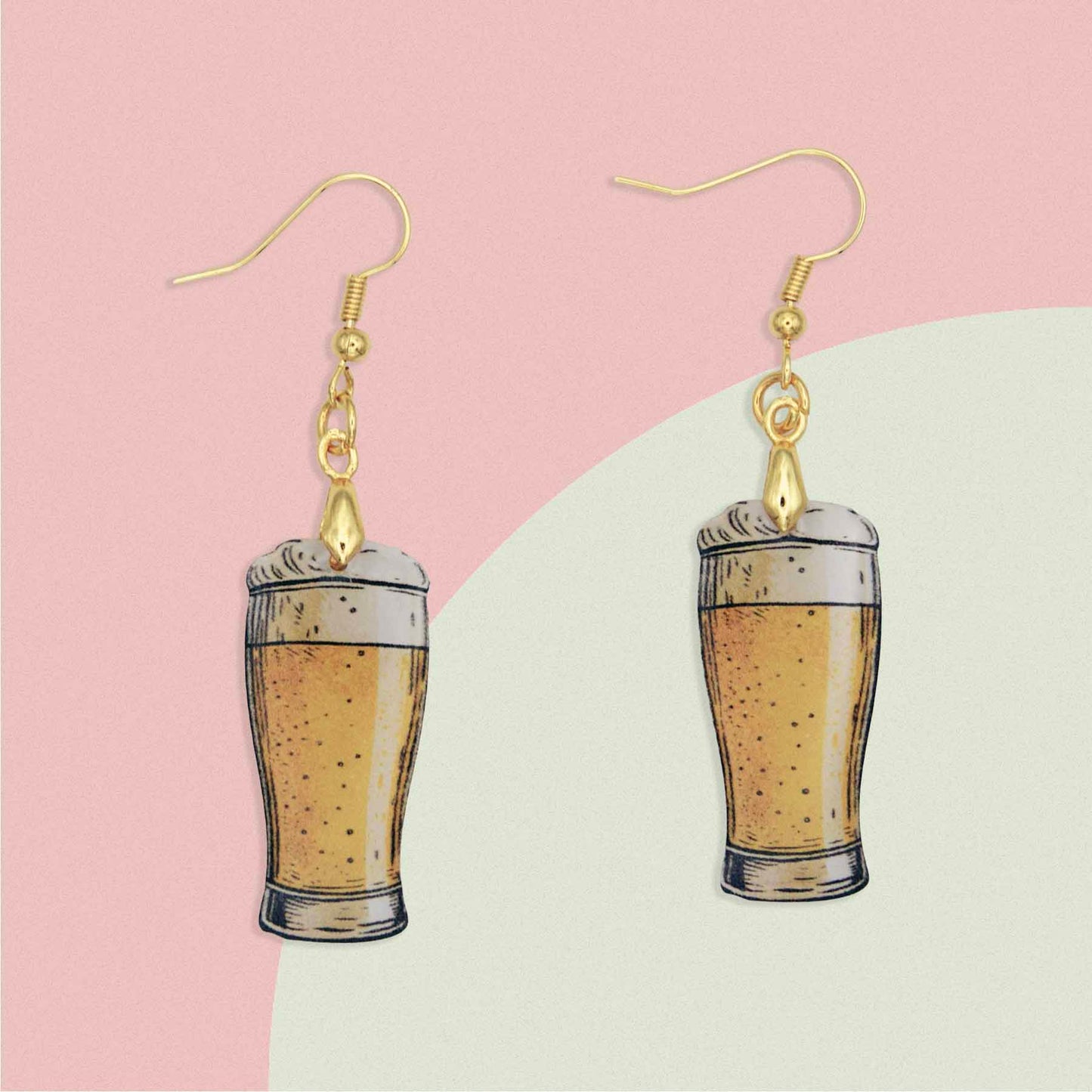 A pair of dangle earrings featuring miniature beer glasses filled with golden ale and foamy heads, suspended from gold-colored hooks.