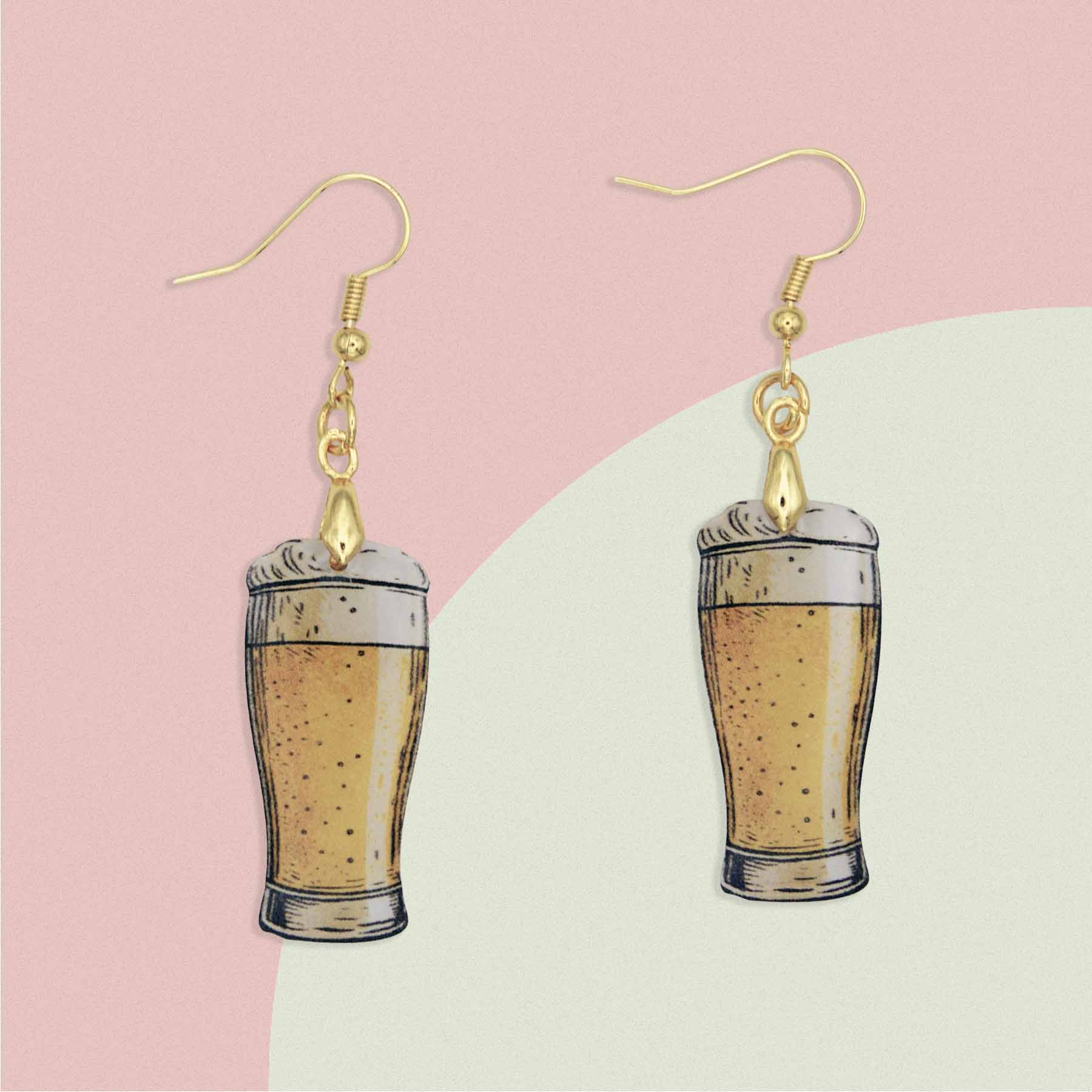 A pair of dangle earrings featuring miniature beer glasses filled with golden ale and foamy heads, suspended from gold-colored hooks.