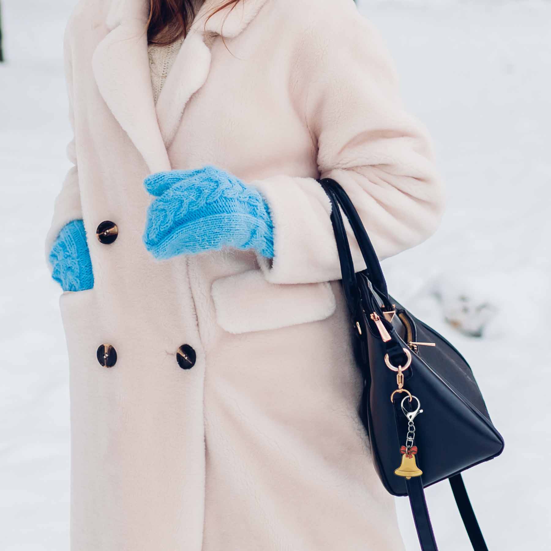 Christmas jingle bell bag charm keychain on a black purse, shown with a person in a cream coat and blue mittens.