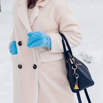 Christmas jingle bell bag charm keychain on a black purse, shown with a person in a cream coat and blue mittens.