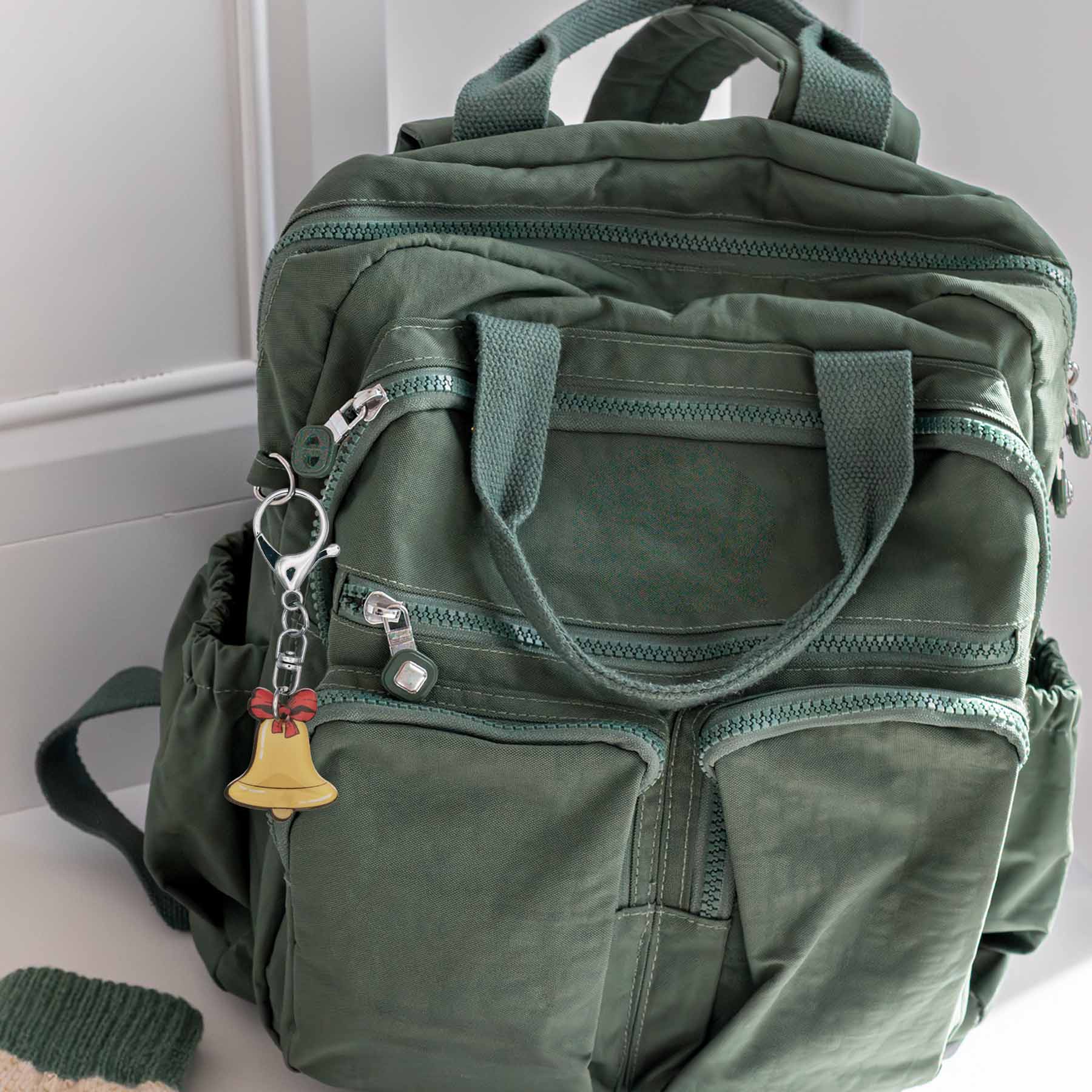 Christmas jingle bell bag charm keychain with red bow, attached to a green backpack, showcasing its golden bell forrest green backpack.