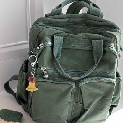 Christmas jingle bell bag charm keychain with red bow, attached to a green backpack, showcasing its golden bell forrest green backpack.