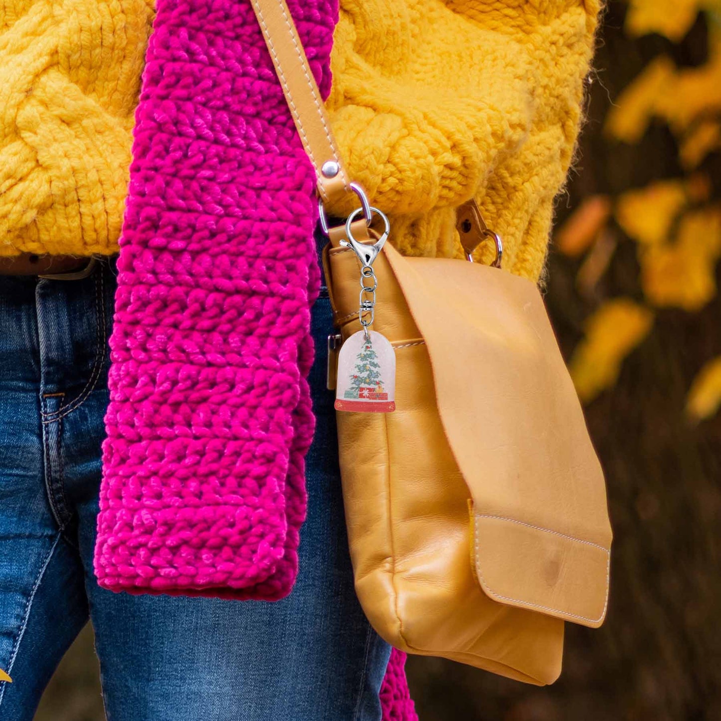 Christmas snow globe bag charm keychain on a tan purse, showing a festive tree and presents inside.