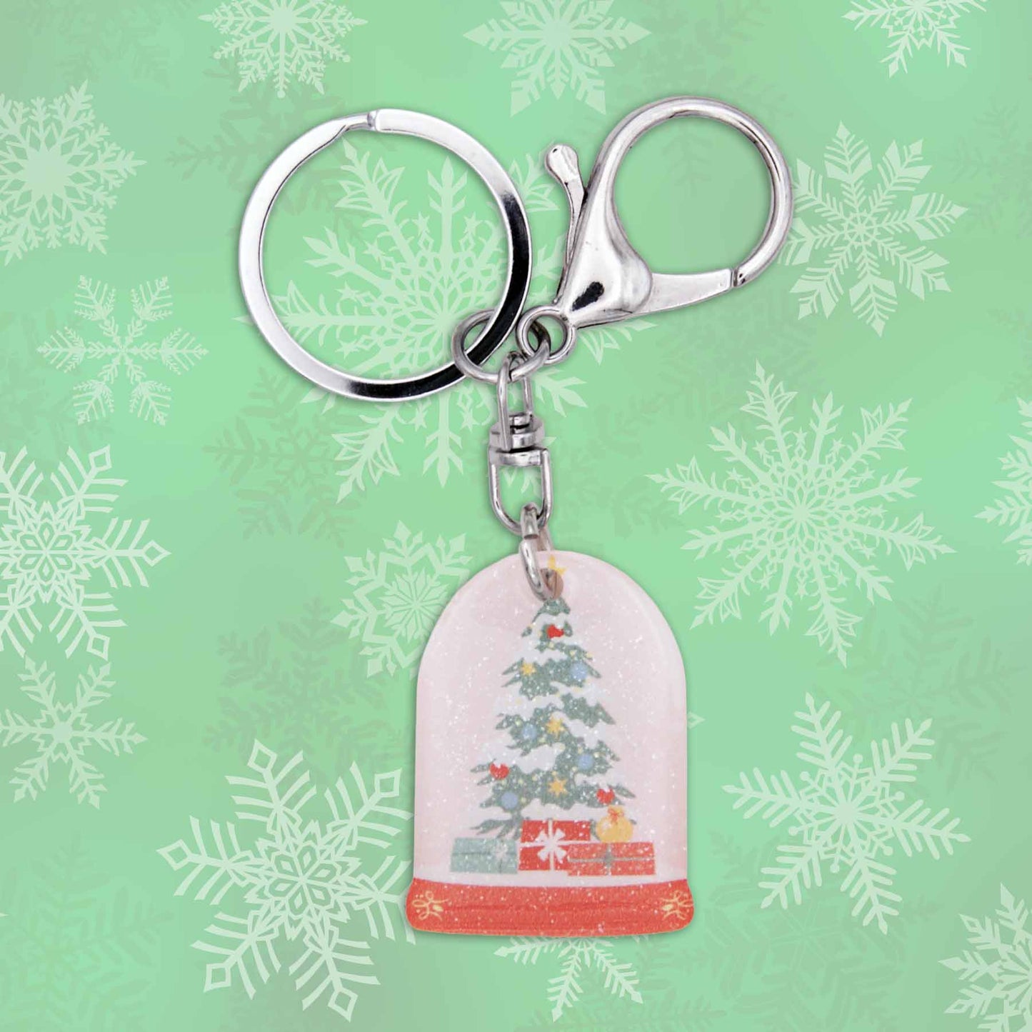 Christmas snow globe bag charm keychain with silver keyring and clasp on a green snowflake background.