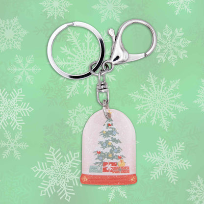 Christmas snow globe bag charm keychain with silver keyring and clasp on a green snowflake background.