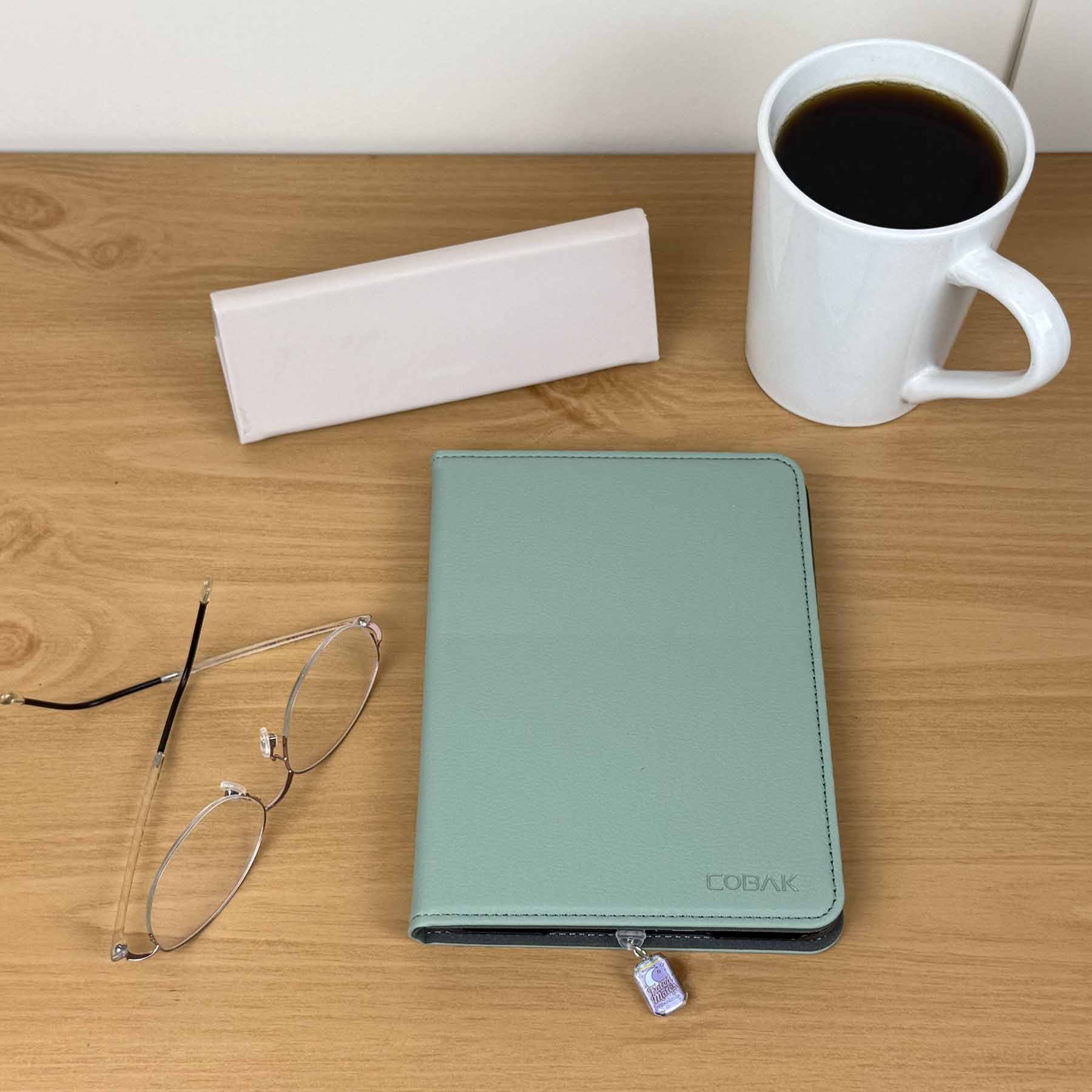 Fated Mate Soda Can Kindle Charm attached to a light blue Kindle cover, next to reading glasses and a coffee mug.