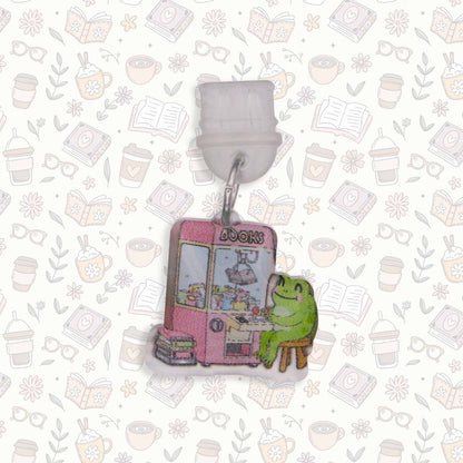 Frog & Claw Machine Kindle Charm USB-C dust plug. Cute frog sits by pink 'BOOKS' claw machine on decorative background.