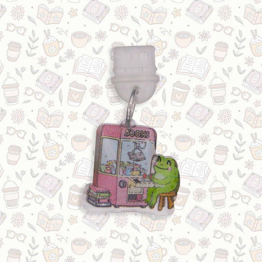 Frog & Claw Machine Kindle Charm USB-C dust plug. Cute frog sits by pink 'BOOKS' claw machine on decorative background.