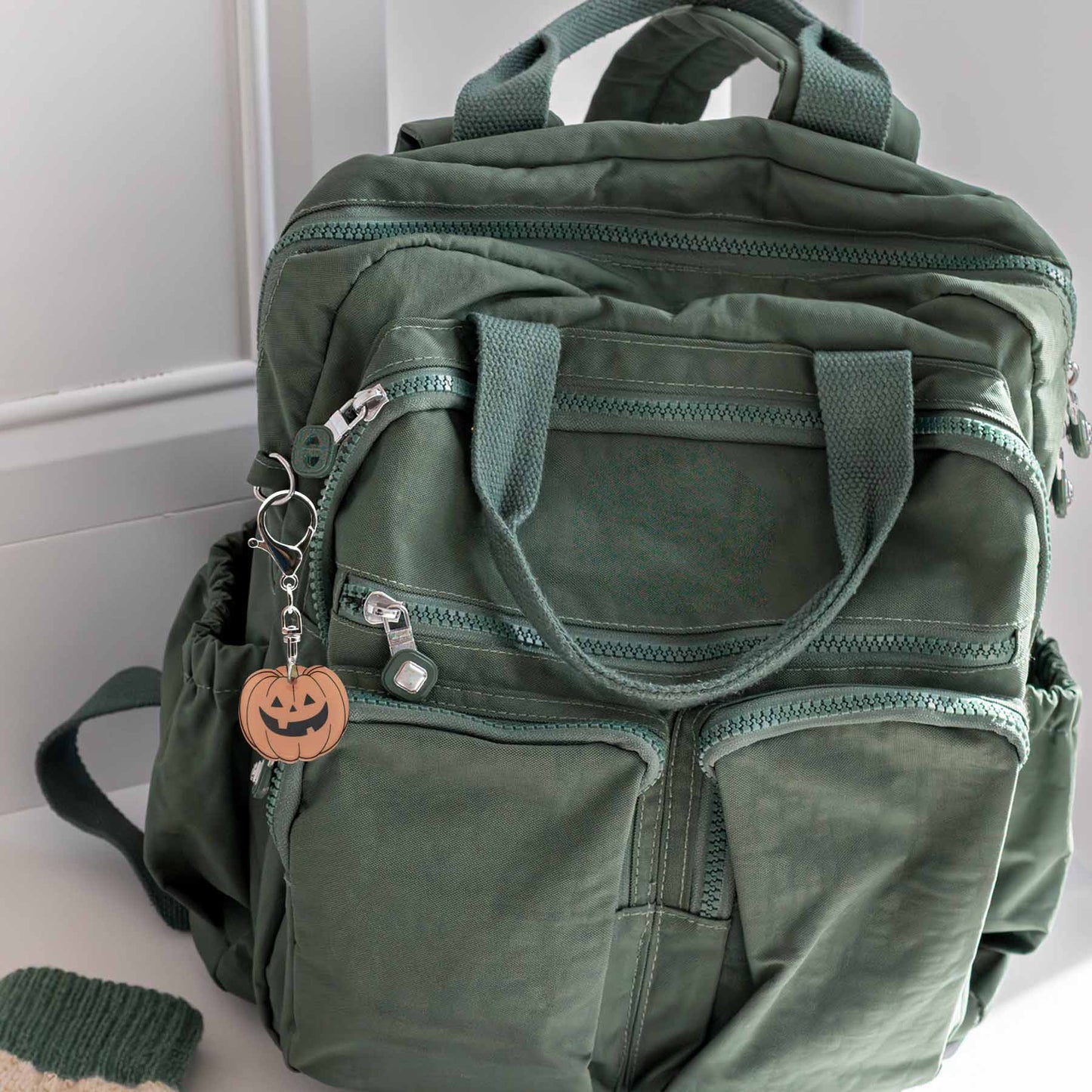 Green backpack with multiple zippered pockets and a Halloween pumpkin keychain attached to a zipper pull.