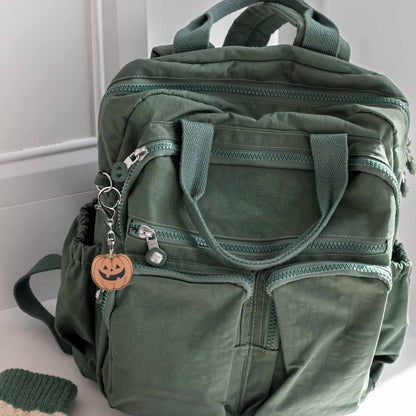 Green backpack with multiple zippered pockets and a Halloween pumpkin keychain attached to a zipper pull.