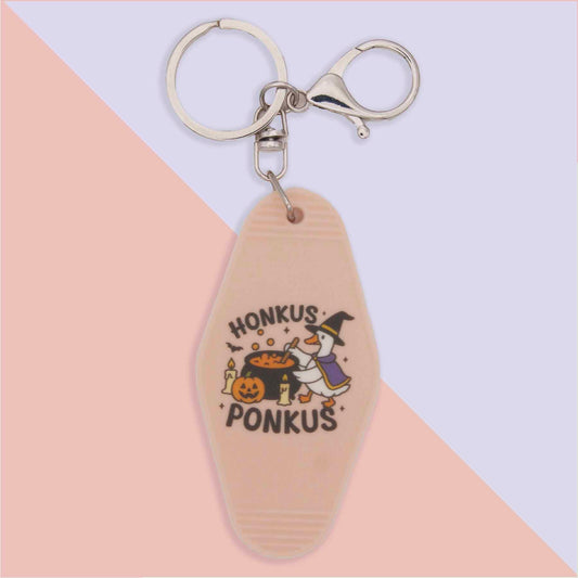 Honkus Ponkus Halloween keychain with a witch duck stirring a cauldron, alongside a pumpkin and candles.