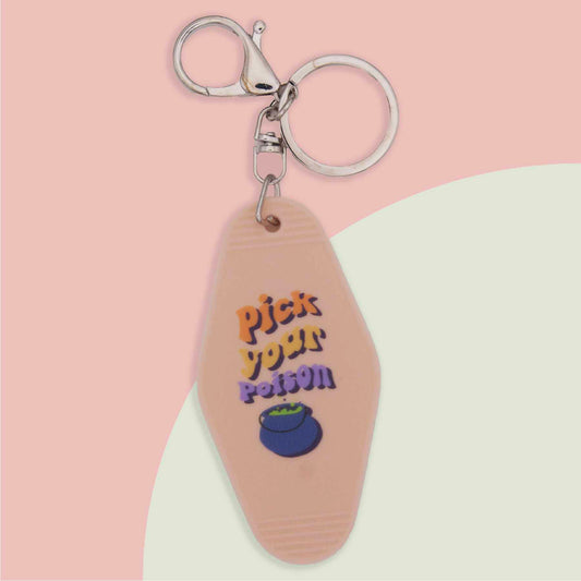 Peach colored hotel-style keychain with "Pick Your Poison" in colorful text, a blue cauldron, and a silver keyring.