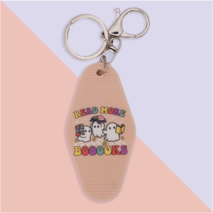 Tan motel-style keychain with silver hardware. Features three cartoon ghosts and the text 'READ MORE BOOOOKS'. One ghost holds books, another wears glasses, and the third reads a book.