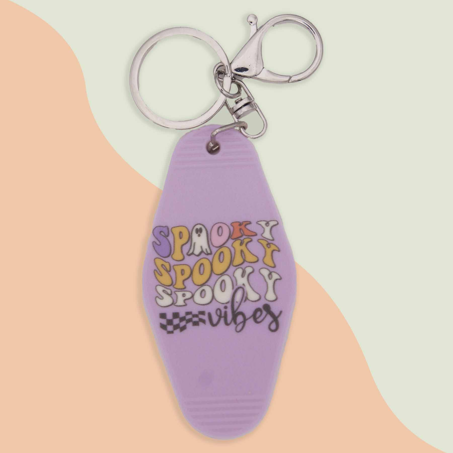 Lavender motel-style keychain with 'Spooky Spooky Spooky Vibes' text in purple, orange, and black, featuring ghost and checkered flag details.