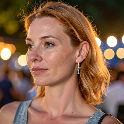 Woman wearing a margarita cocktail glass earring, featuring a lime slice detail, against a blurred background of festive lights.