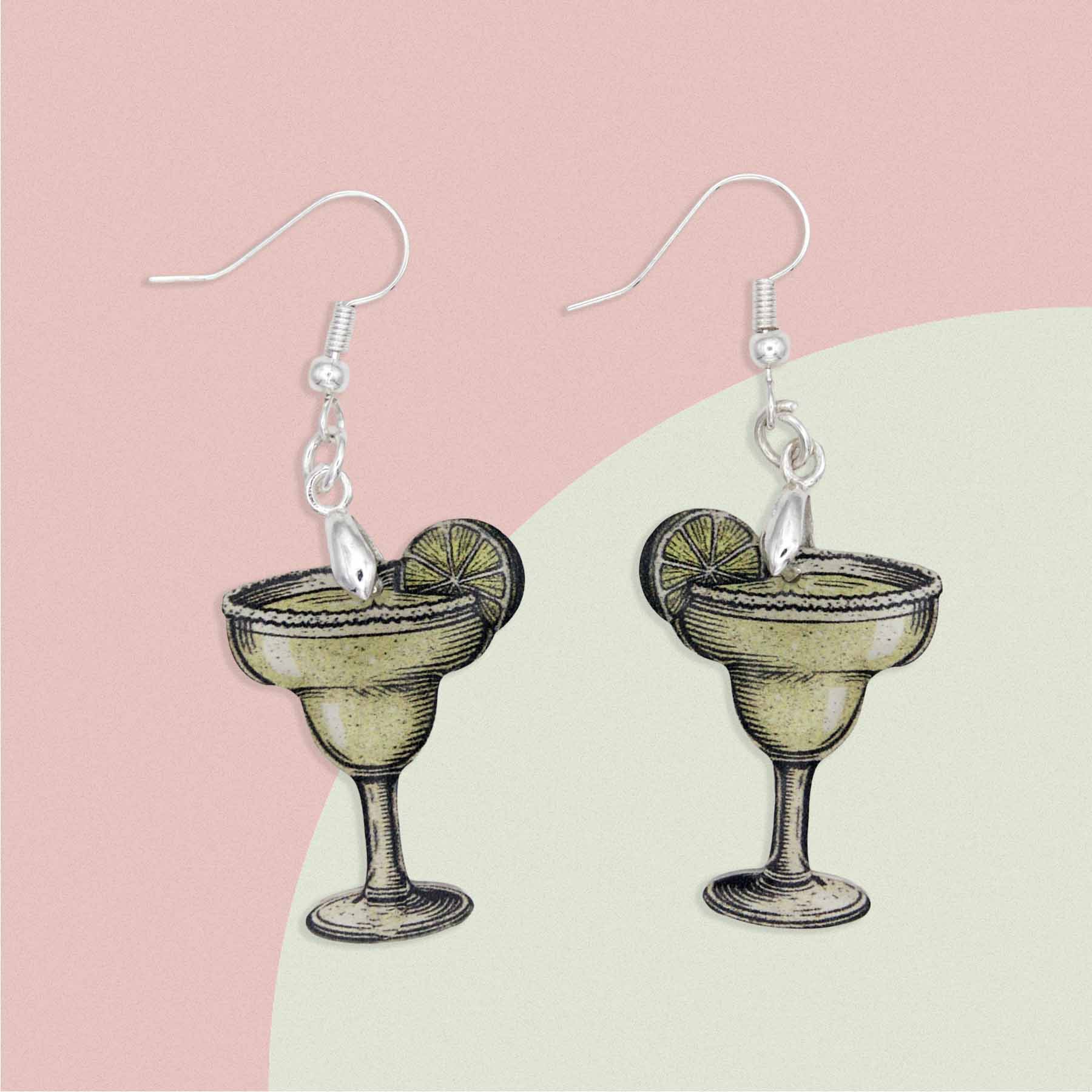 Pair of margarita cocktail drop earrings with lime slice detail and silver hooks on a pink and green background.
