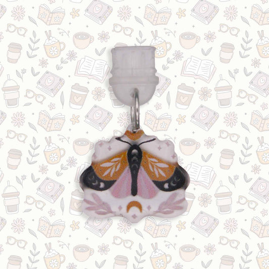 Moth Kindle Charm, a USB-C dust plug, with intricate moth design in pink, black, and gold colors