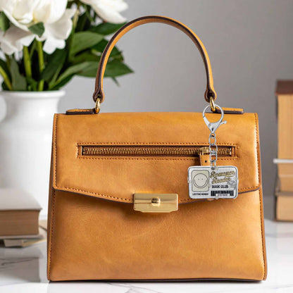 Romance Reader Book Club library card keychain hanging from a brown leather handbag. The keychain is white with a smiling face, text "Romance Reader BOOK CLUB," "LIFETIME MEMBER," and a barcode.
