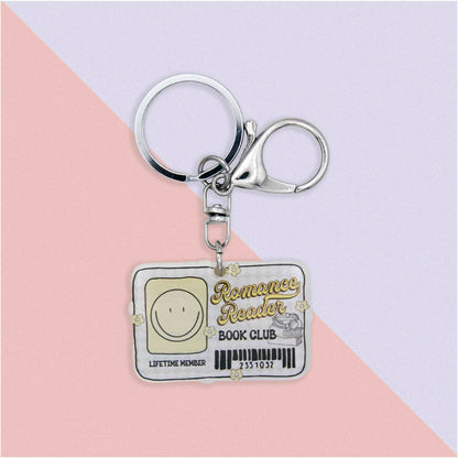 Romance Reader Book Club Lifetime Member keychain with a smiley face icon, books, and flowers, on a pink and white background.