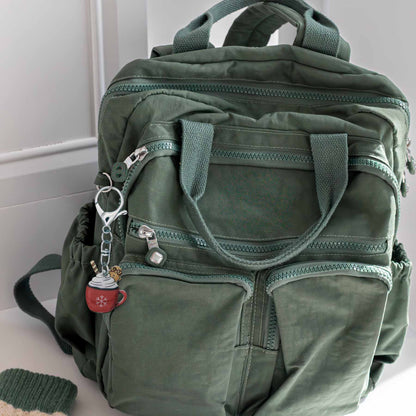 Winter hot cocoa bag charm keychain with snowflake design attached to a green backpack, a green backpack