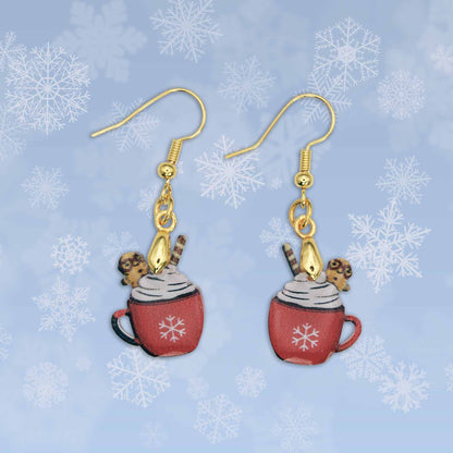 A pair of dangle earrings featuring red hot cocoa mugs with snowflakes, topped with whipped cream, a wafer stick, and a gingerbread man, set against a light blue snowflake background.