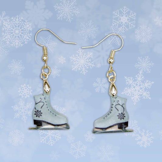 A pair of light blue ice skate dangle earrings with black floral designs. Gold-toned hooks are attached to the top of each skate, which feature black blades and black heels.