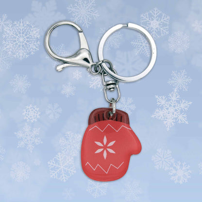 Red acrylic winter mitten bag charm keychain with a snowflake design, silver clasp, and keyring on a snowy background.