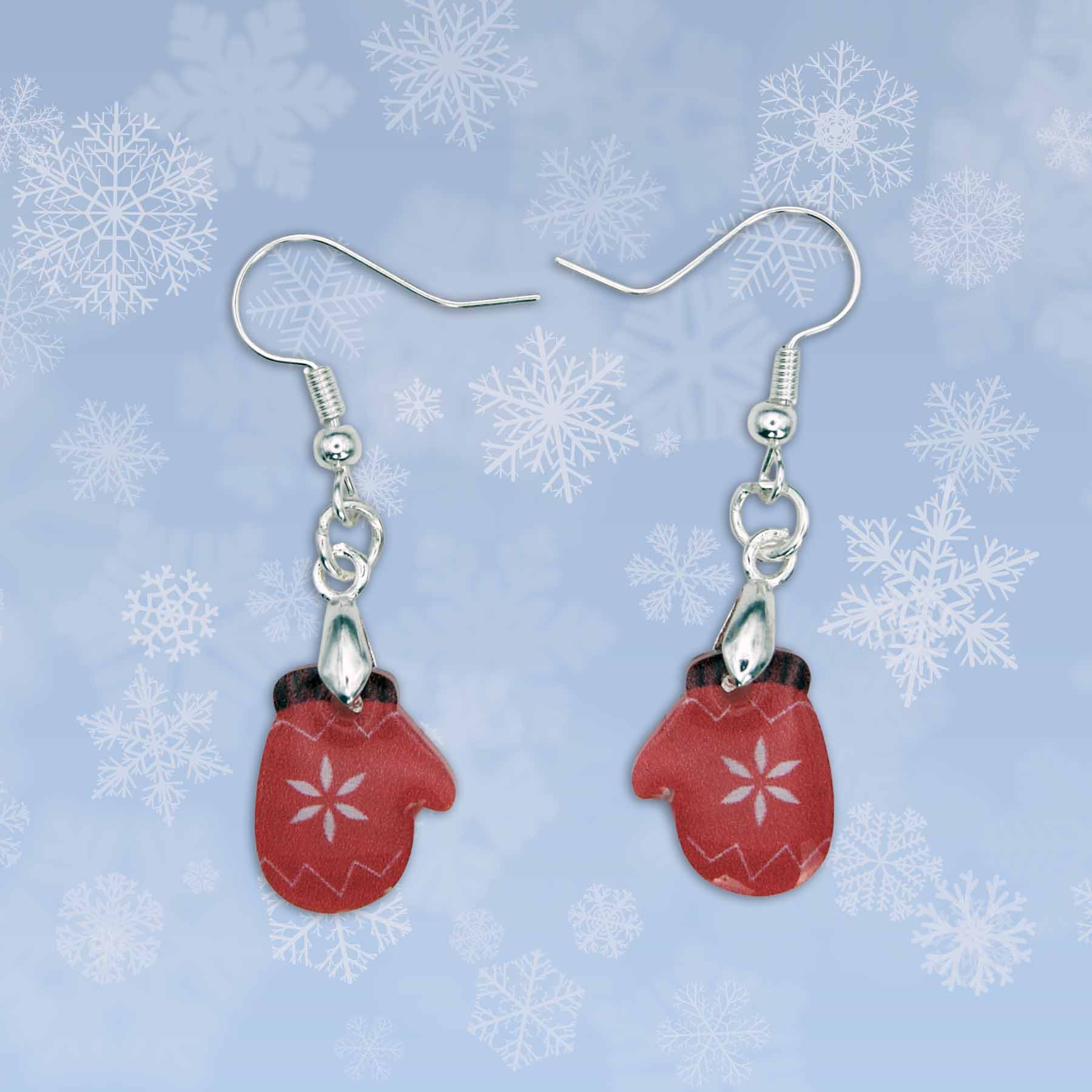 A pair of red mitten earrings with white snowflake designs, hanging from silver hooks against a light blue snowflake background.