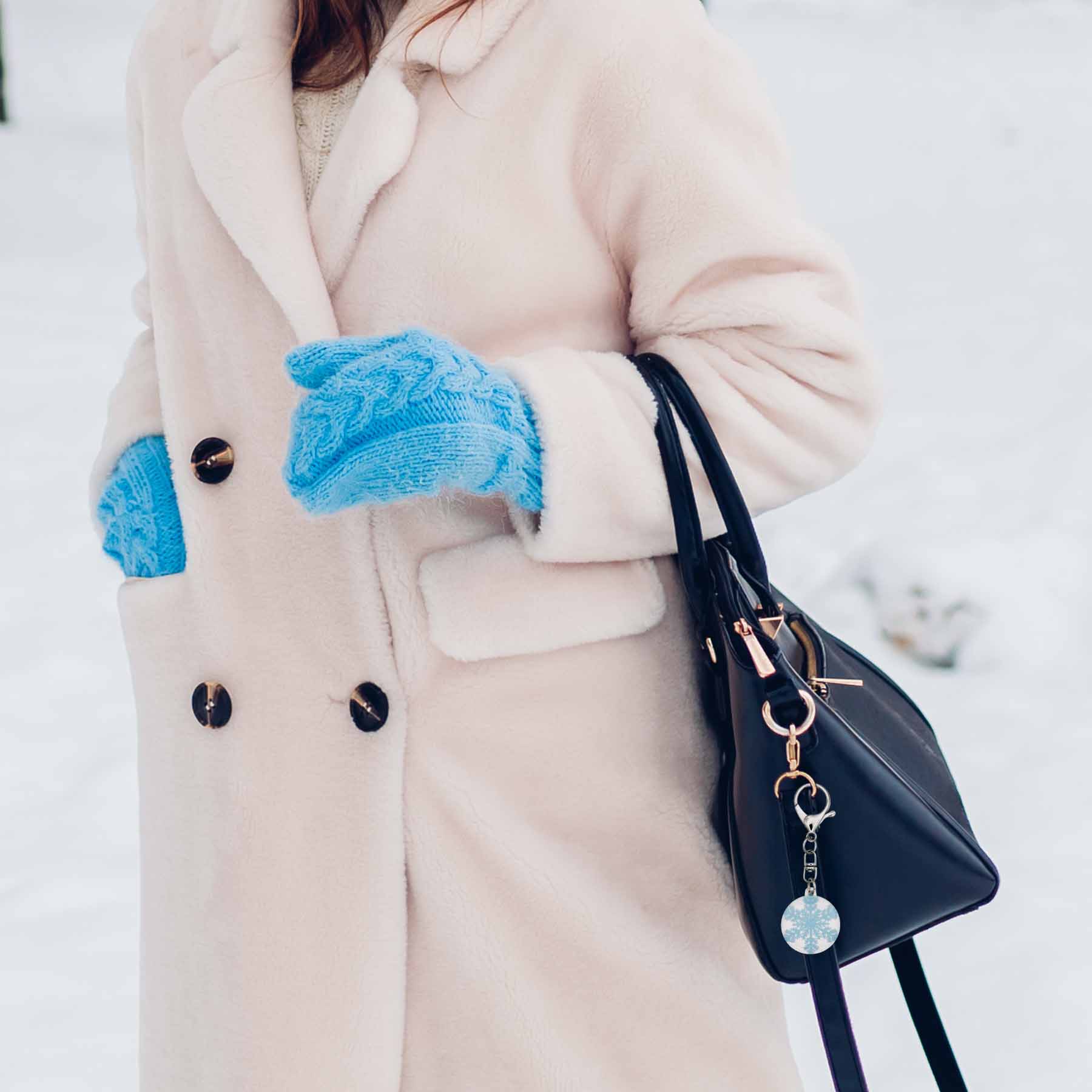 Sparkly snowflake bag charm keychain on a black purse, worn by a person in a cream coat and blue mittens.