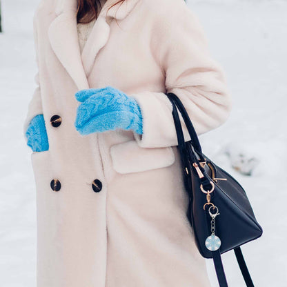 Sparkly snowflake bag charm keychain on a black purse, worn by a person in a cream coat and blue mittens.