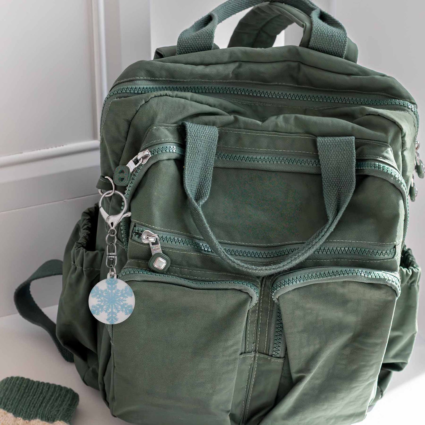 Sparkly Snowflake Bag Charm Keychain with silver clasp and keyring, attached to a green backpack.