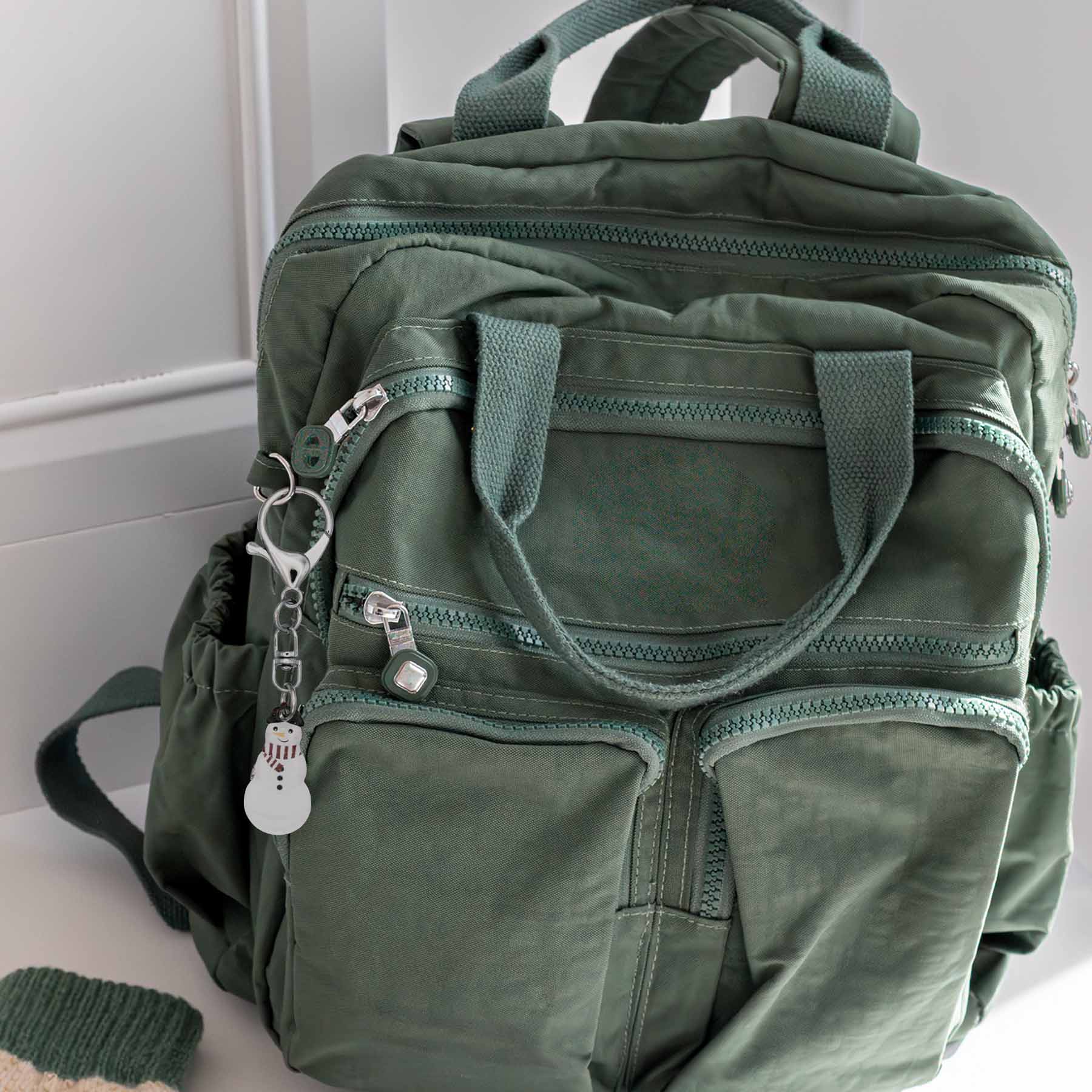 Snowman bag charm keychain with a silver clasp, attached to a green backpack, showcasing its versatility as a versatile accessory.